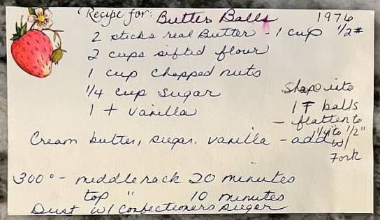 A handwritten recipe card on a stone counter — “Recipe for: Butter Balls, 1976” in blue cursive on cream stock, with a strawberry painted in one corner.